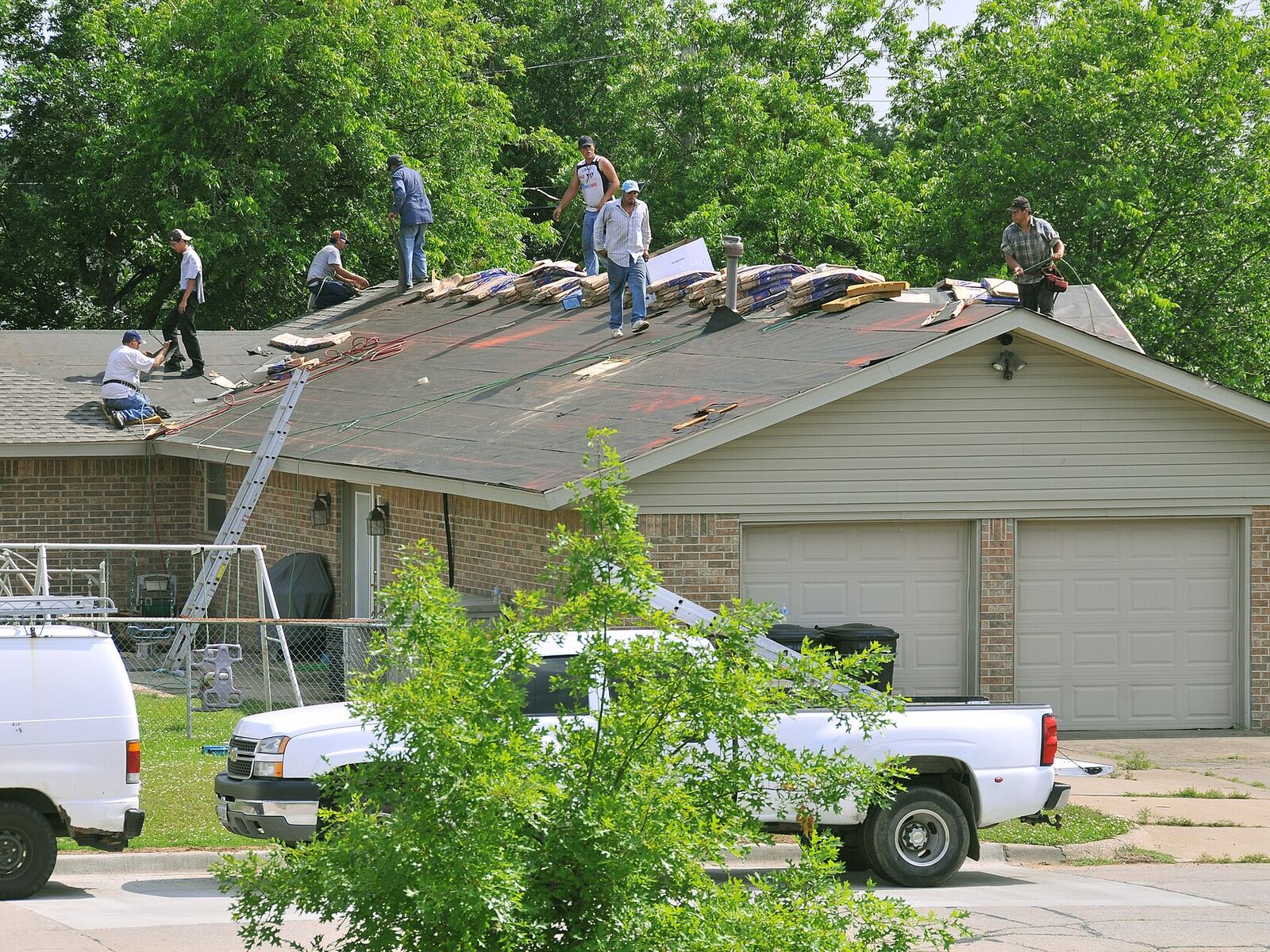 Roofing crew tearing off and replacing asphalt shingles on a single-story home